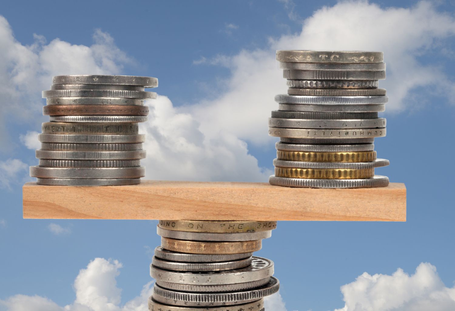 Coins stabilized on a see saw in front of a cloudy blue-sky background. Representing Environmental Services Financial Stability.